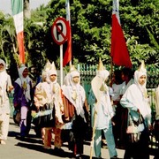 Van veraf lijkt het een Ku-Klux-Klan-optocht maar als ze dichterbij komen zie ik dat ze de gebruikelijke witte hoofddoek dragen en daar bovenop een witte puntmuts hebben gezet. Een feestmuts om precies te zijn. Omstanders leggen me uit dat het hier een feestelijke schooloptocht betreft ter gelegenheid van het einde van het schooljaar.