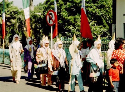 Van veraf lijkt het een Ku-Klux-Klan-optocht maar als ze dichterbij komen zie ik dat ze de gebruikelijke witte hoofddoek dragen en daar bovenop een witte puntmuts hebben gezet. Een feestmuts om precies te zijn. Omstanders leggen me uit dat het hier een feestelijke schooloptocht betreft ter gelegenheid van het einde van het schooljaar.