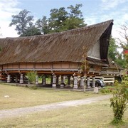 Het koningshuis van de Batak Simalungung. Op een open plaats in het bos staat een wel dertig meter lang huis op palen met een fraai puntdak.    