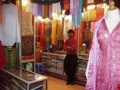 In de bazaar is een winkelgalerij vol van de prachtigste sjaals en japonnen in felle kleuren. De Indiase eigenaar van één van de winkels poseert trots.
