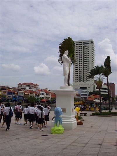 Raffles op de plek waar hij in 1819 aan land kwam. De schoolkinderen hebben zich met hem laten fotograferen. Achter het beeld een Travellers Palm, waaiervorming.    