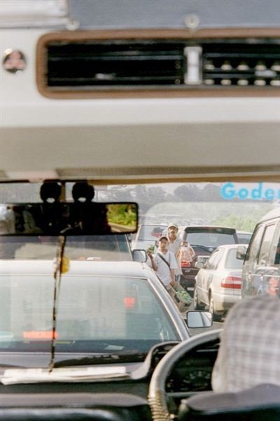 File op de snelweg op de vroege zaterdagochtend. Bedelaars en verkopers van koekjes begeven zich langs de stilstaande auto's om wat handel los te wrikken.    