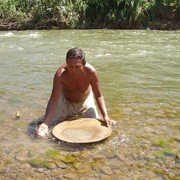 Een goudzoeker in de rivier Mais. Hij schept wat zand uit de rivier in de schaal en voegt daar steeds handjes water bij terwijl hij de schaal heen en weer beweegt.    