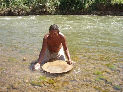 Een goudzoeker in de rivier Mais. Hij schept wat zand uit de rivier in de schaal en voegt daar steeds handjes water bij terwijl hij de schaal heen en weer beweegt.