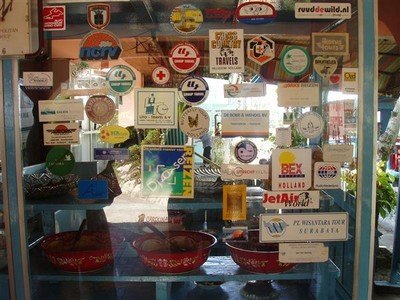 Stickers op de vitrine van Pondok Flora. "Waar zouden we zijn zonder de trein?" staat op de NS-sticker (midden boven). Hier kennelijk.